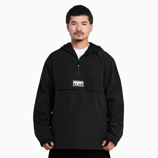 A man wearing a black hooded pullover anorak jacket with a half-zip neckline and a white chest patch reading 'PRO CLUB.' 