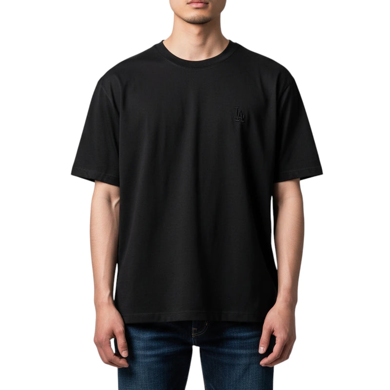 Load image into Gallery viewer, A man wearing a black short-sleeve crewneck t-shirt with a small tonal black embroidered logo on the left chest, paired with blue jeans, against a plain white background.
