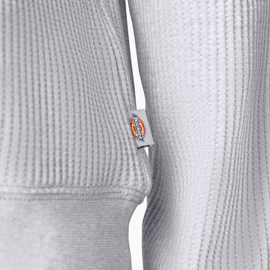 Close up of the side logo and knit of the Dickies Women's Thermal Crewneck Shirt - Light Heather Gray - This ashy gray thermal shirt features a classic waffle knit fabric thermal is perfect for wearing on its own or layered under your favorite Dickies hoodies and jackets.