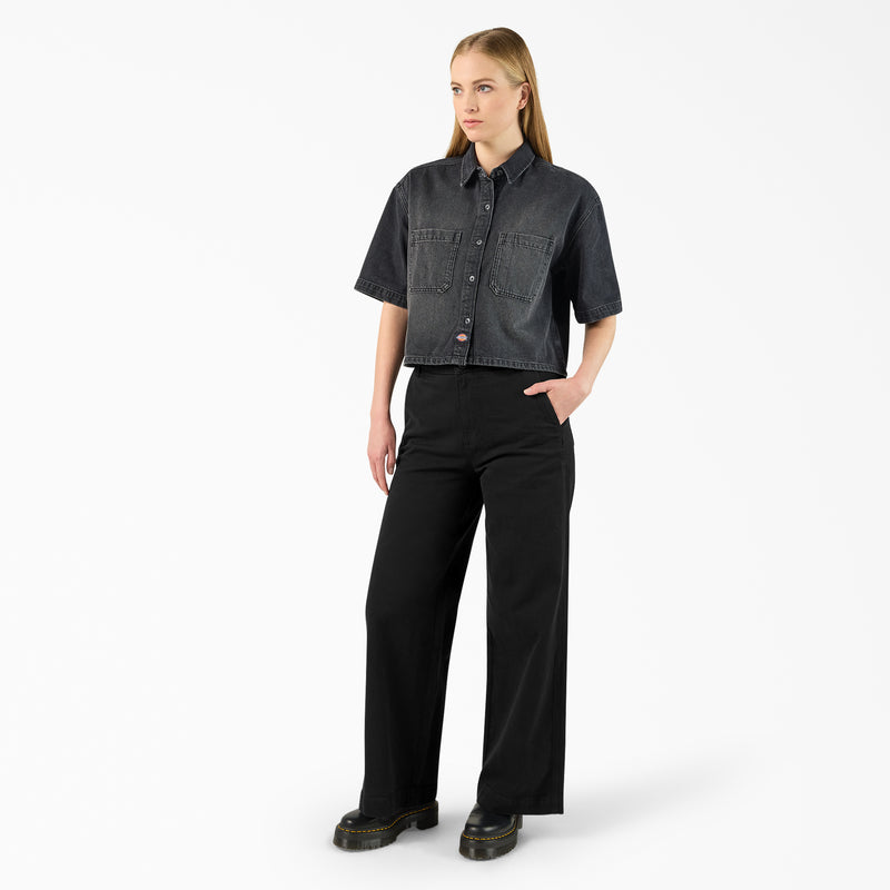 Load image into Gallery viewer, A model wearing a black boxy, cropped women's Dickies denim short sleeve work shirt that is sandwashed for vintage look and a worn-in feel.
