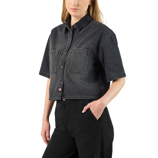 A model wearing a black boxy, cropped women's Dickies denim short sleeve work shirt that is sandwashed for vintage look and a worn-in feel.
