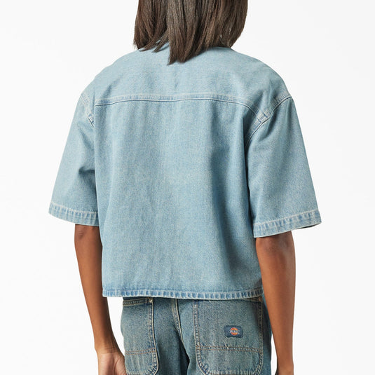 The back of a model wearing a light blue boxy, cropped women's Dickies denim short sleeve work shirt that is sandwashed for vintage look and a worn-in feel.