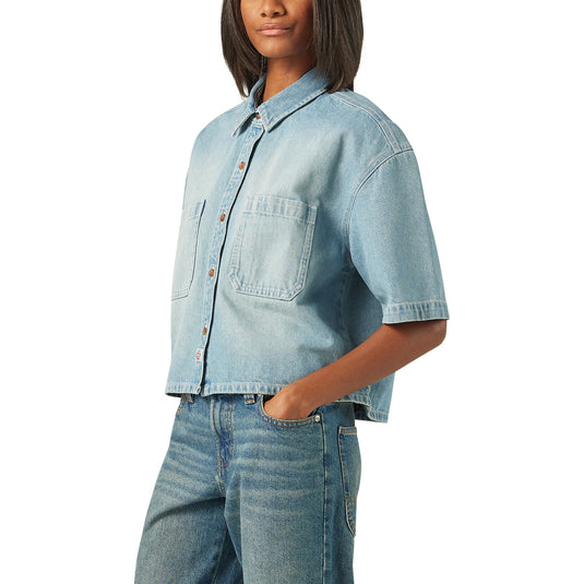 A model wearing a light blue boxy, cropped women's Dickies denim short sleeve work shirt that is sandwashed for vintage look and a worn-in feel.