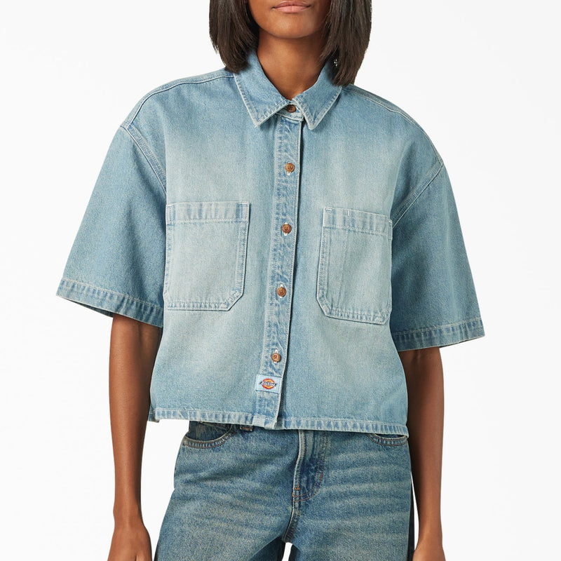 Load image into Gallery viewer, A model wearing a light blue boxy, cropped women's Dickies denim short sleeve work shirt that is sandwashed for vintage look and a worn-in feel.

