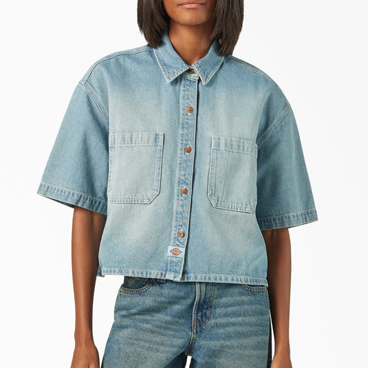 A model wearing a light blue boxy, cropped women's Dickies denim short sleeve work shirt that is sandwashed for vintage look and a worn-in feel.