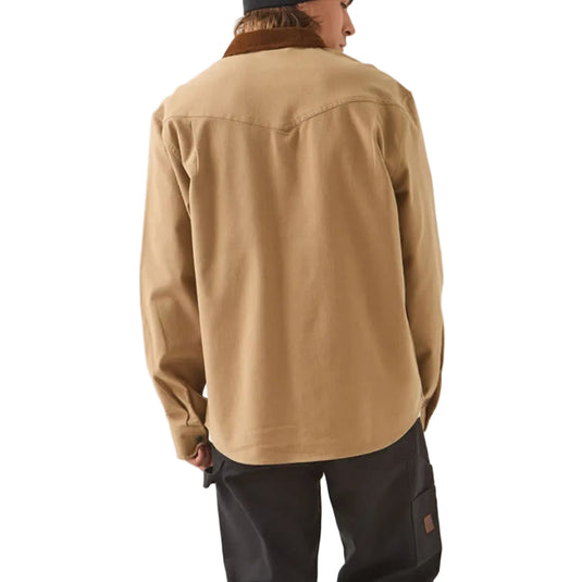 A person shown from the back wearing a tan overshirt, black pants, a black beanie, and black shoes, standing against a plain light gray studio background.