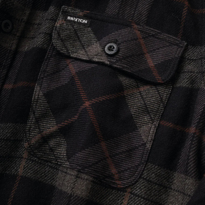 Load image into Gallery viewer, Close-up of a dark plaid flannel shirt pocket with a snap flap. The fabric is black and charcoal gray with thin brown lines, and the Brixton brand label is visible near the top.
