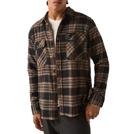 A model wearing a black and brown plaid button-down shirt with a black beanie, standing against a plain off-white background.