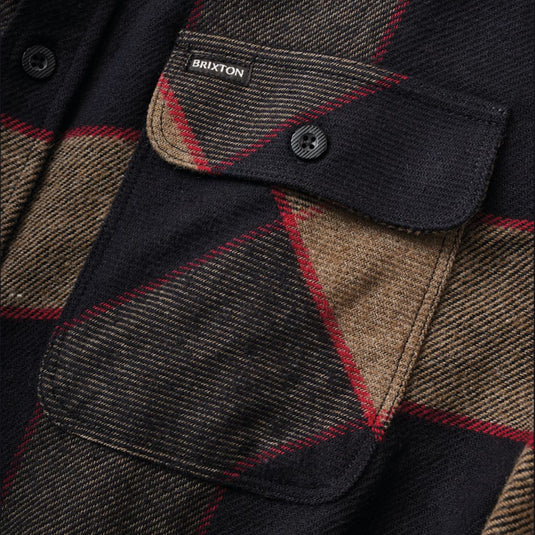 Close-up of a Brixton plaid overshirt featuring a black base with brown and red lines, showing a buttoned chest pocket with a visible Brixton label.