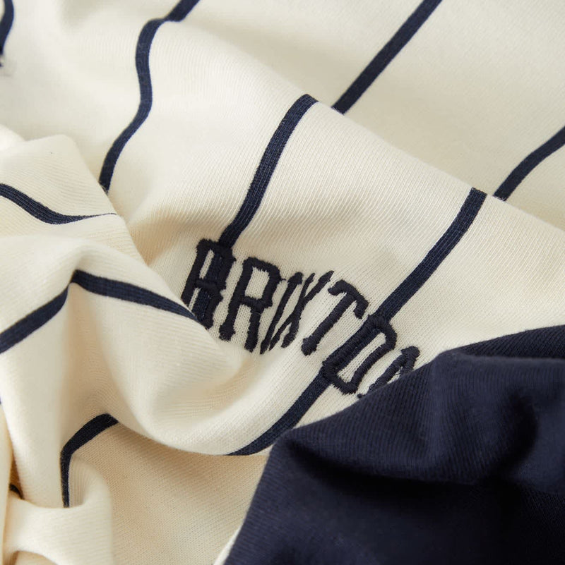 Load image into Gallery viewer, Close-up of a cream-colored fabric garment with navy blue vertical stripes and a matching navy blue solid section, featuring the partial embroidered text 'BRITON'.
