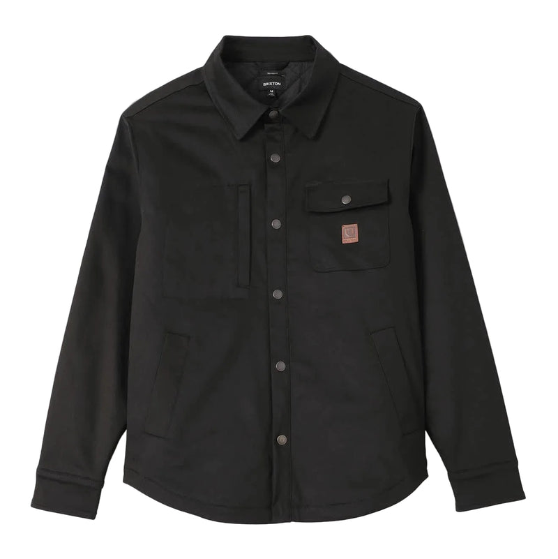 Load image into Gallery viewer, A black long-sleeve button-up overshirt jacket with a pointed collar, two chest flap pockets, and a small brown leather Brixton logo patch on the left chest, displayed on a light gray background.
