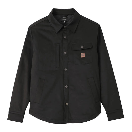 A black long-sleeve button-up overshirt jacket with a pointed collar, two chest flap pockets, and a small brown leather Brixton logo patch on the left chest, displayed on a light gray background.