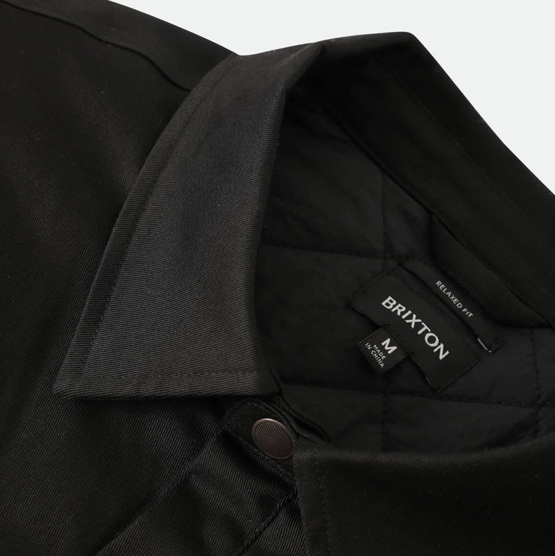 Load image into Gallery viewer, Close-up of a black collared shirt jacket with a buttoned front and a visible BRIXTON neck label.
