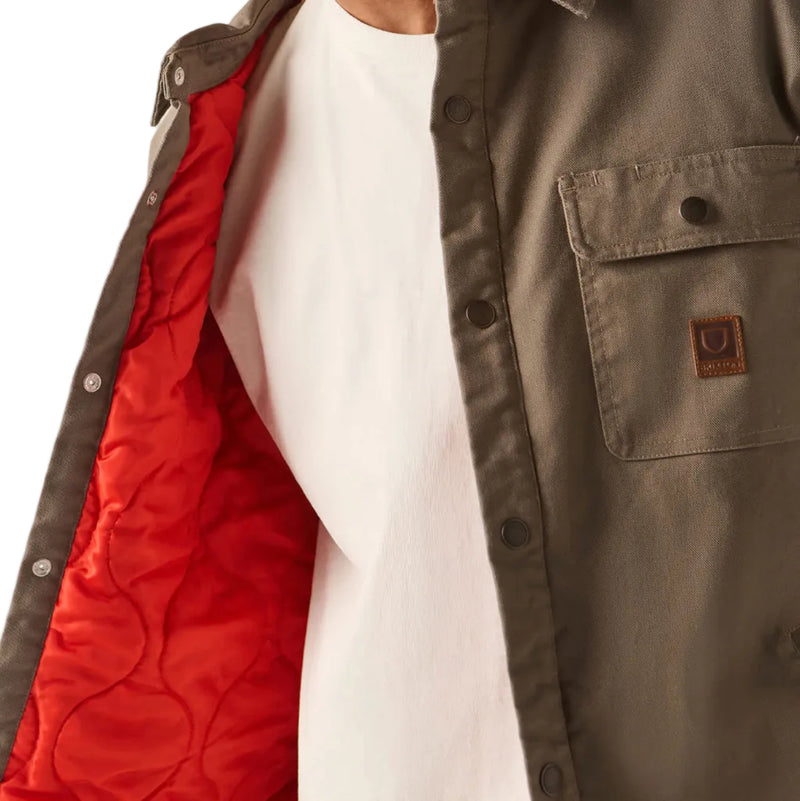 Load image into Gallery viewer, A close-up side profile of a person wearing a brown overshirt with a bright red quilted lining, layered over a white t-shirt and a red-and-white baseball cap.
