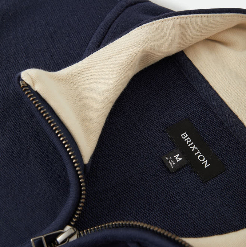 Load image into Gallery viewer, Close-up of a navy blue zip-up garment with a cream-colored inner collar lining and a visible black Brixton brand label.
