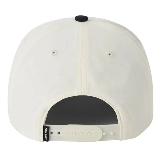 Back view of a cream-colored snapback cap with a black button on top and an adjustable strap with a small black BRIXTON brand tag.