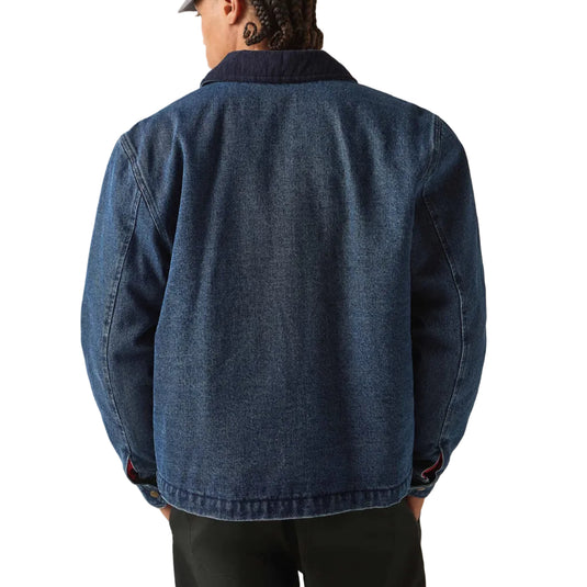 A person shown from the back wearing a dark blue denim jacket, black pants, and a gray cap against a plain light beige studio background.
