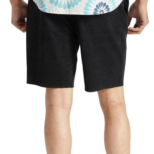 A person wearing black knee-length shorts, shown from the waist down against a light gray studio background. The shorts have a relaxed fit and side pockets.