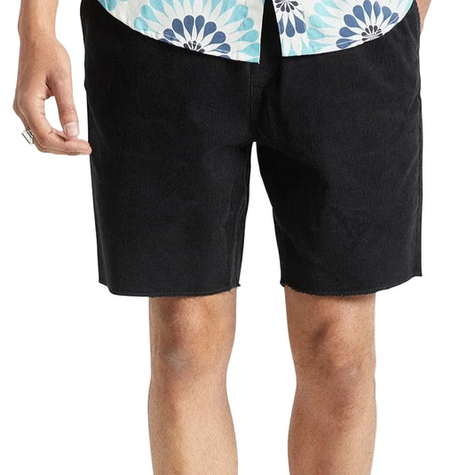 A person wearing black shorts, white socks, and black sneakers, cropped from the waist down against a light gray studio background.
