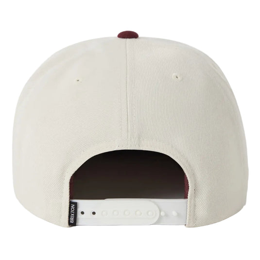 Back view of a off white snapback cap with a burgundy button and white adjustable strap on a white background.