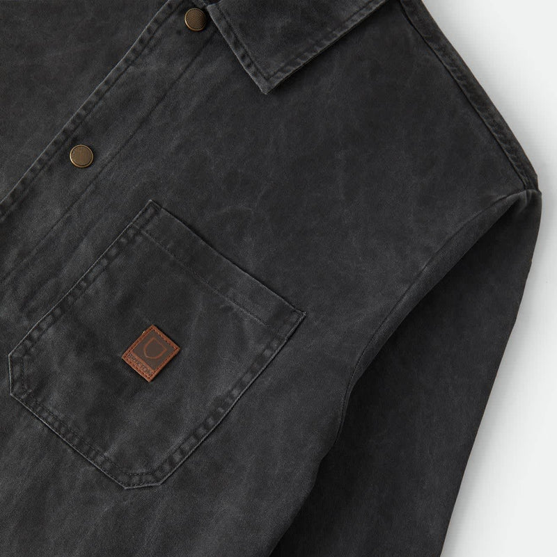 Load image into Gallery viewer, Close-up of a dark charcoal gray waxed cotton shirt jacket with a chest pocket and a small brown leather brand patch.
