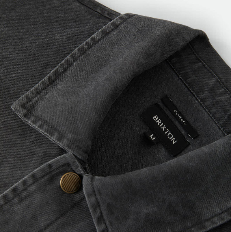Load image into Gallery viewer, Close-up of a dark charcoal gray washed denim overshirt collar with a single brass button and a visible BRIXTON neck label.
