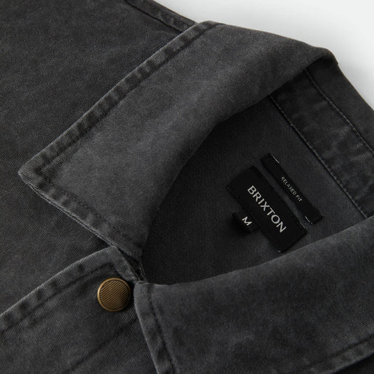 Close-up of a dark charcoal gray washed denim overshirt collar with a single brass button and a visible BRIXTON neck label.