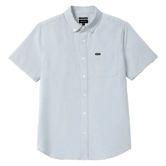A light blue gray short-sleeve button-down shirt with a chest pocket and a small black logo patch on the left chest, displayed against a light gray background.
