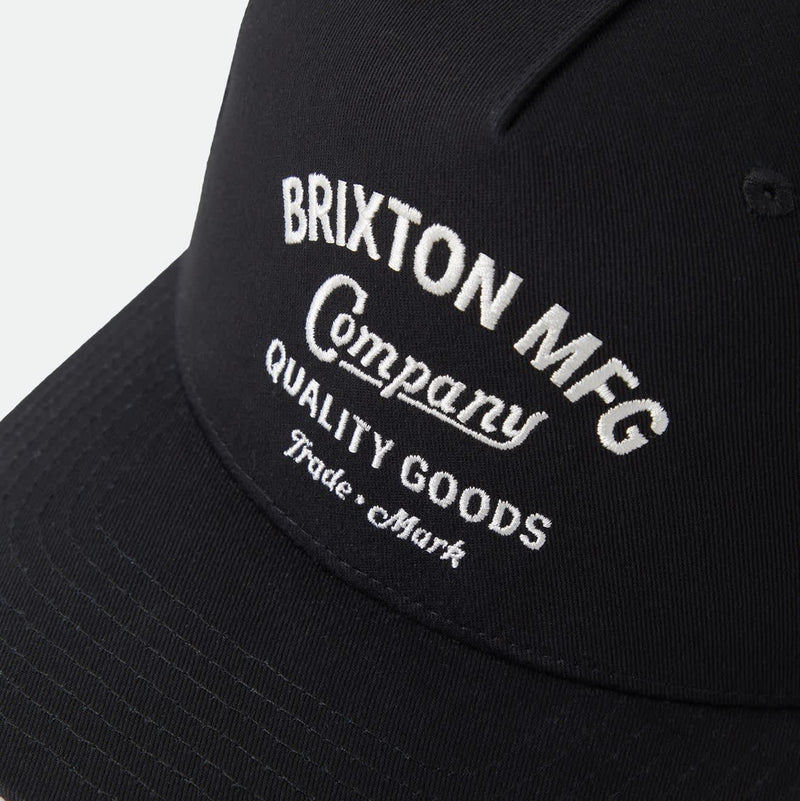 Load image into Gallery viewer, A close-up of a black baseball cap featuring white embroidered text that reads 'BRIXTON MFG Company QUALITY GOODS Trade Mark' on a light gray background.
