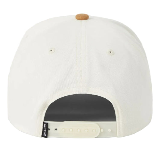 The back of a structured baseball cap in off-white, featuring a small tan button on top, ventilation eyelets, and an adjustable snapback closure with a black brand tag.