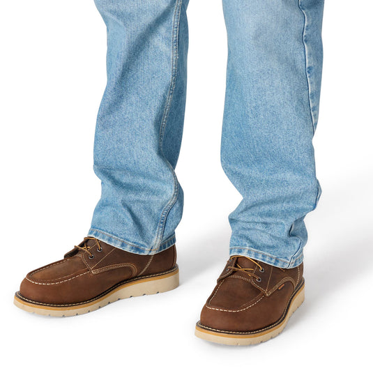 A close-up of a person's legs wearing light blue jeans and brown suede boat shoes with tan soles, shown against a plain white background.