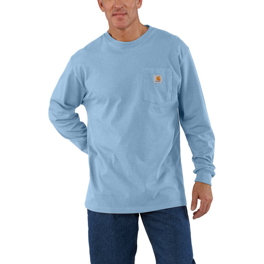 A man wearing a light blue long-sleeve pocket t-shirt with a small Carhartt logo on the chest pocket, paired with dark blue jeans, against a plain white background.