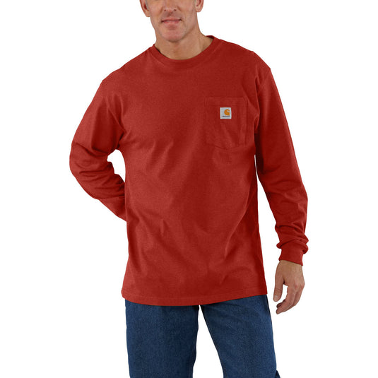 A man wearing a red long-sleeve pocket t-shirt with a small Carhartt logo patch on the chest, paired with blue jeans, against a plain white background.