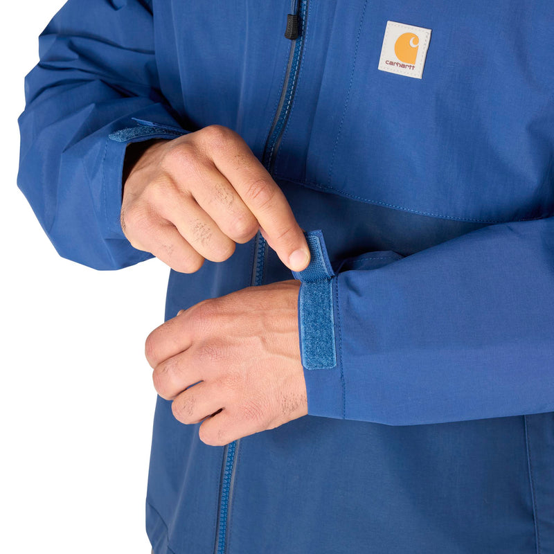 Load image into Gallery viewer, Close-up of a person wearing a blue Carhartt jacket, demonstrating the adjustable hook-and-loop cuff strap on the sleeve.
