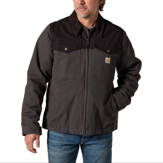A man wearing a dark brown Carhartt work jacket with a zip-up front, chest pockets, and a signature Carhartt logo patch on the left chest, paired with blue jeans against a plain white background.