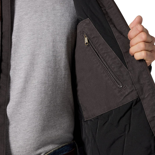 Close-up of a person wearing a dark charcoal gray jacket over a heather gray shirt, with a hand holding open the jacket to show a zippered pocket.