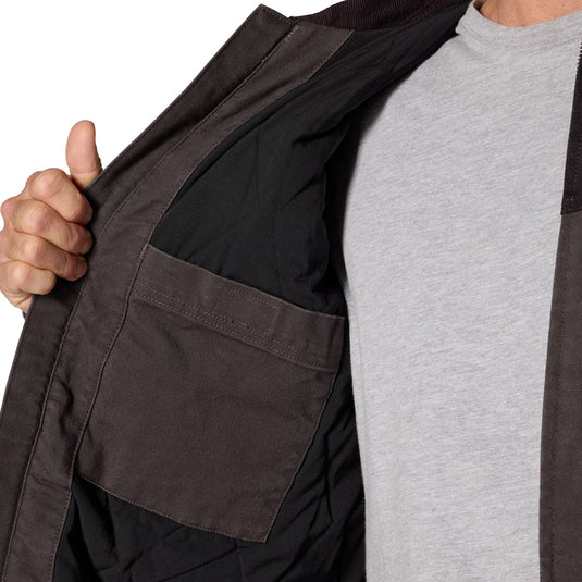 Close-up of a person wearing a dark brown utility jacket over a light gray t-shirt, with the hand opening the jacket to show the black interior lining and pocket.