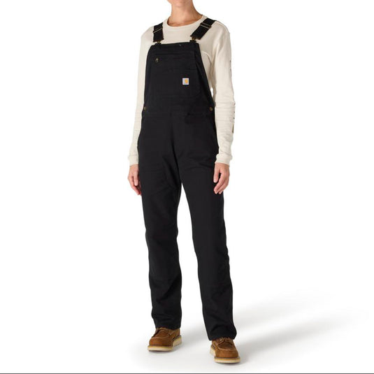 Woman wearing black overalls and a cream long-sleeve shirt underneath on a white background