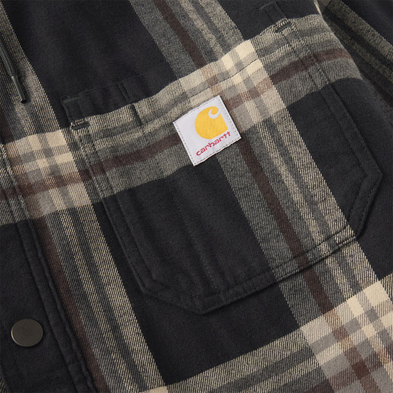 Load image into Gallery viewer, Close-up of a Carhartt plaid overshirt jacket in black, beige, and brown, featuring a front chest pocket with the signature yellow Carhartt logo patch.
