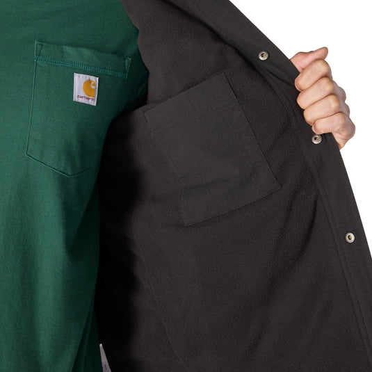 Close-up of a person wearing a dark charcoal zip-front overshirt over a green Carhartt shirt, with the hand holding open the overshirt to show the pocket and snap buttons.