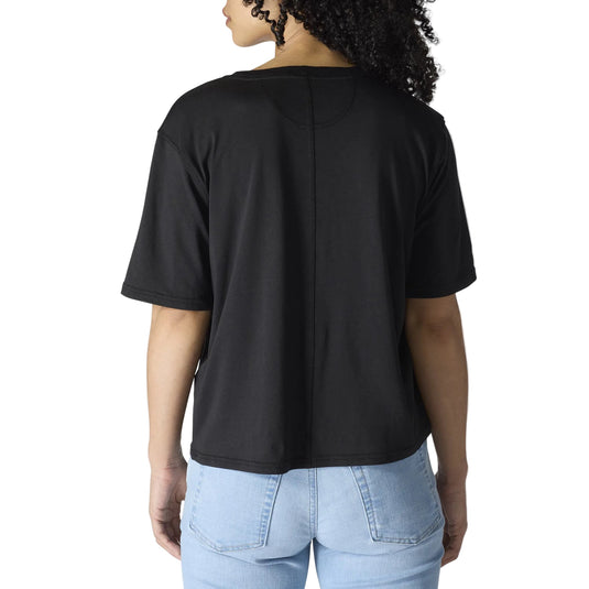 A person shown from the back wearing a black short-sleeve cropped T-shirt and light blue jeans against a plain light gray studio background.
