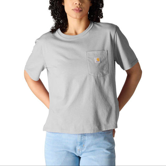 A woman with curly black hair wearing a light gray short-sleeve pocket t-shirt with a small Carhartt logo on the chest pocket, paired with light blue jeans, against a solid white background.