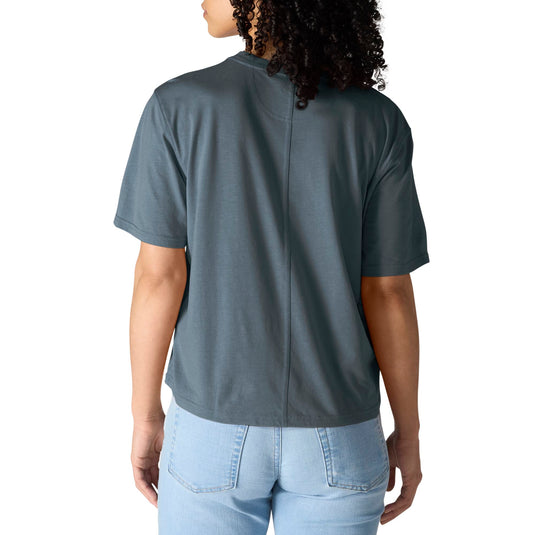 A woman viewed from the back wearing a slate blue-gray short-sleeve t-shirt and light blue jeans against a plain white background.