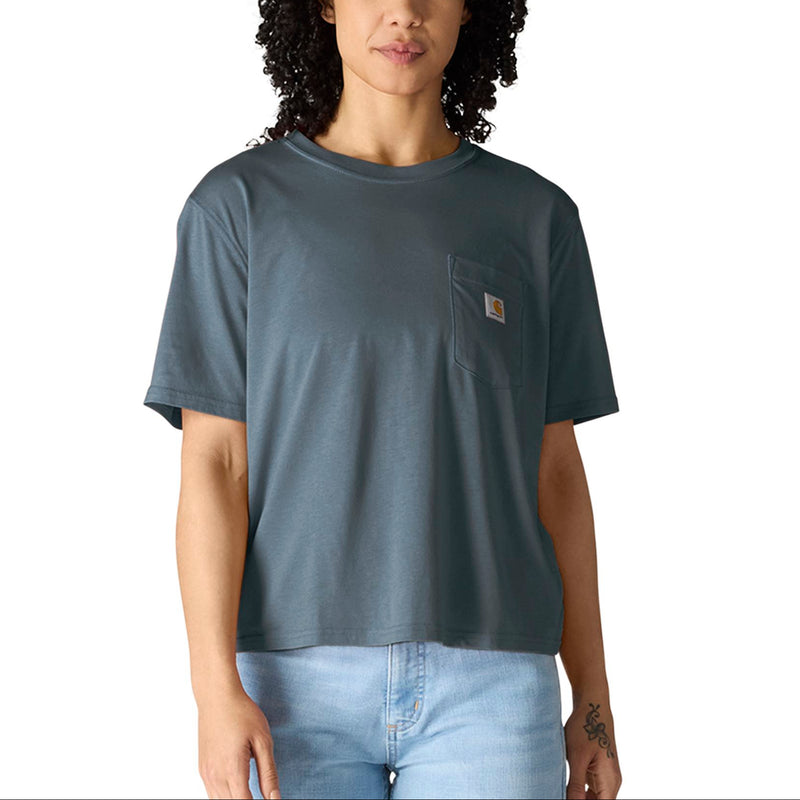 Load image into Gallery viewer, A woman with curly dark hair wearing a muted slate blue-gray short-sleeve pocket t-shirt by Carhartt, paired with light-wash jeans, against a plain white background.
