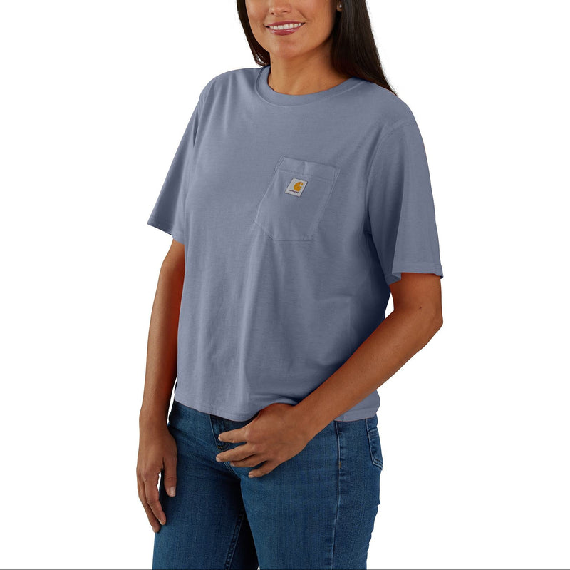 Load image into Gallery viewer, A woman modeling a light blue-gray short-sleeve pocket t-shirt with a small Carhartt logo on the chest pocket, paired with blue jeans against a plain white background.
