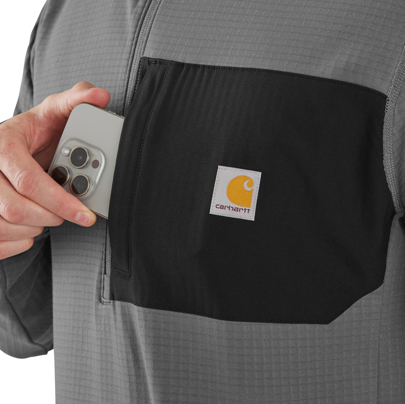Load image into Gallery viewer, Person holding a phone next to a Carhartt logo on a black pocket of a gray jacket.
