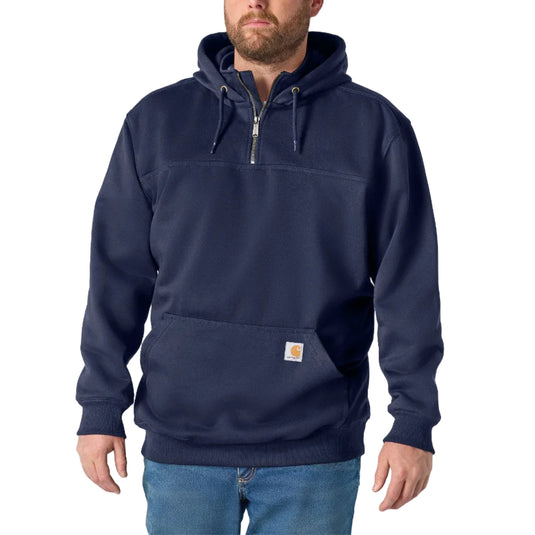 A man wearing a navy blue half-zip pullover hoodie with a drawstring hood and a front kangaroo pocket, paired with blue jeans, against a light gray studio background.