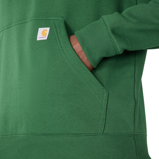 Close-up of a green Carhartt hoodie with a front pocket and a hand reaching into the pocket, showing the Carhartt brand tag.