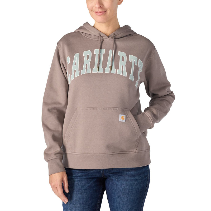 Load image into Gallery viewer, A woman wearing a Carhartt pullover hoodie in taupe with a light green and white varsity-style 'CARHARTTS' graphic across the chest, paired with blue jeans, against a plain white background.
