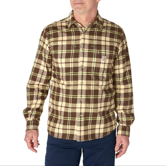 A man wearing a brown and beige plaid long-sleeve button-up shirt with a small Carhartt logo on the chest pocket, paired with navy pants, against a plain white background.